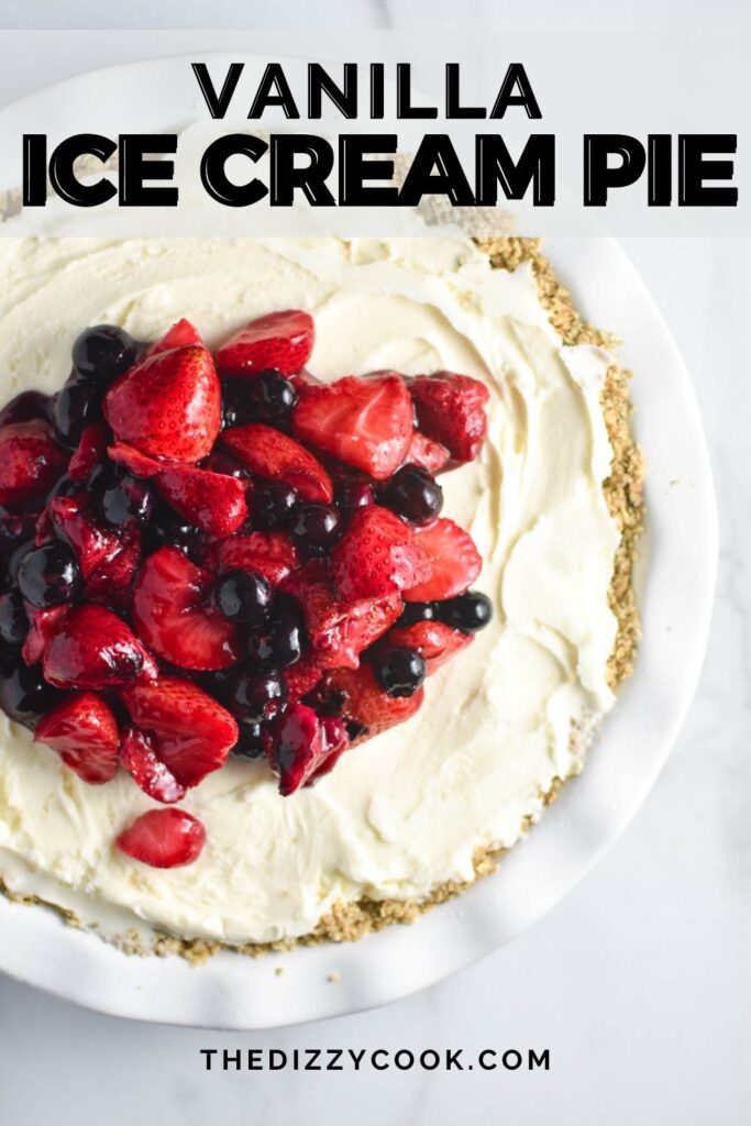 A vanilla ice cream pie on a white table topped with strawberries and blueberries