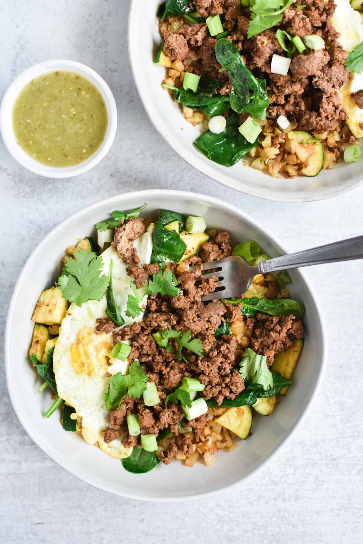 A fork digging into a beef protein bowl with salsa verde.