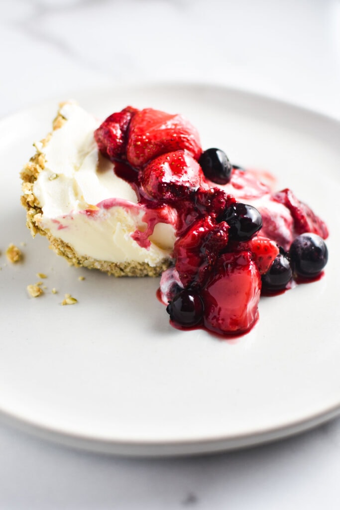 A slice of ice cream pie melting on a plate with berries on top