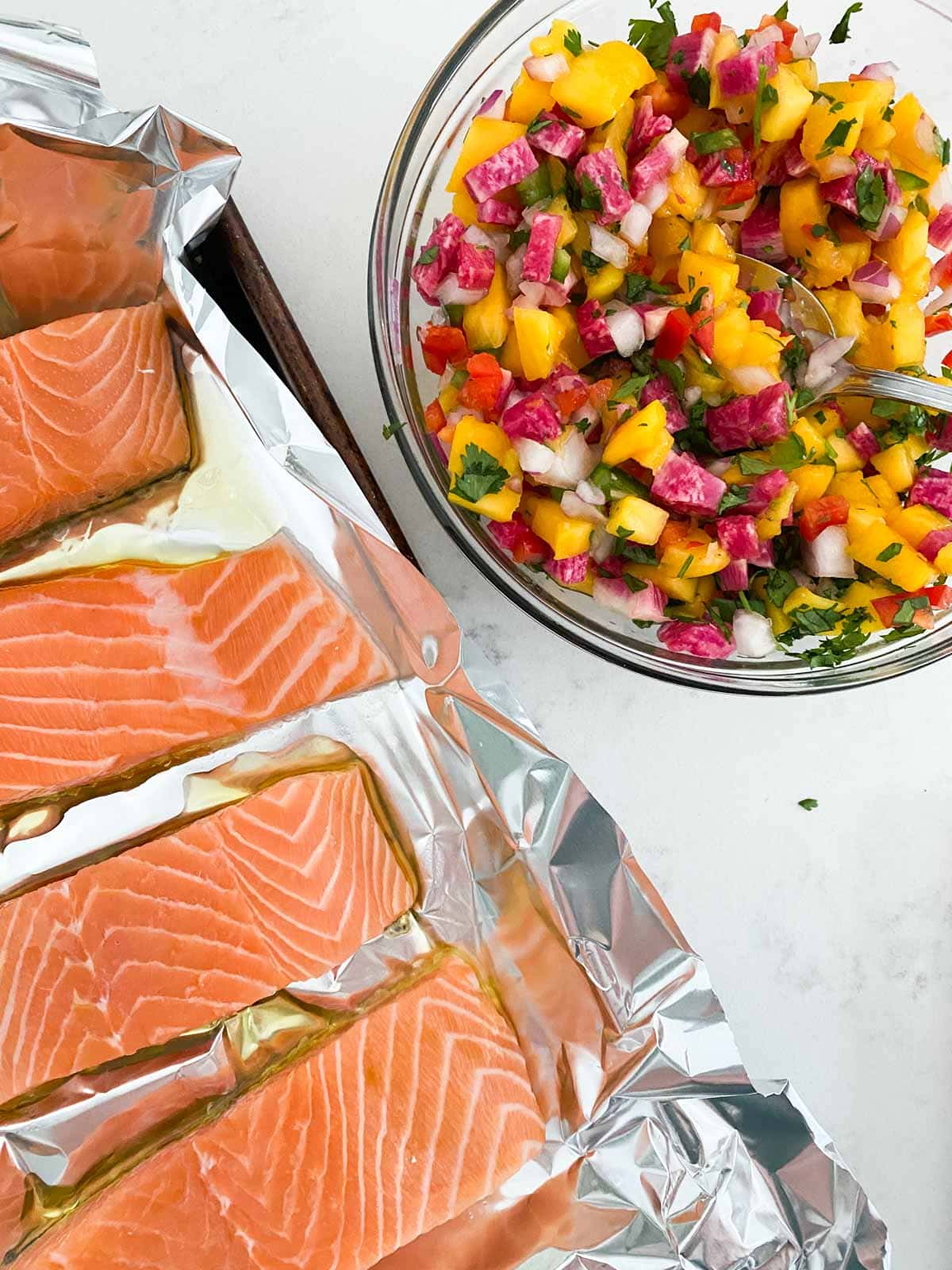 Raw salmon on a sheet pan next to a bowl of mango salsa.