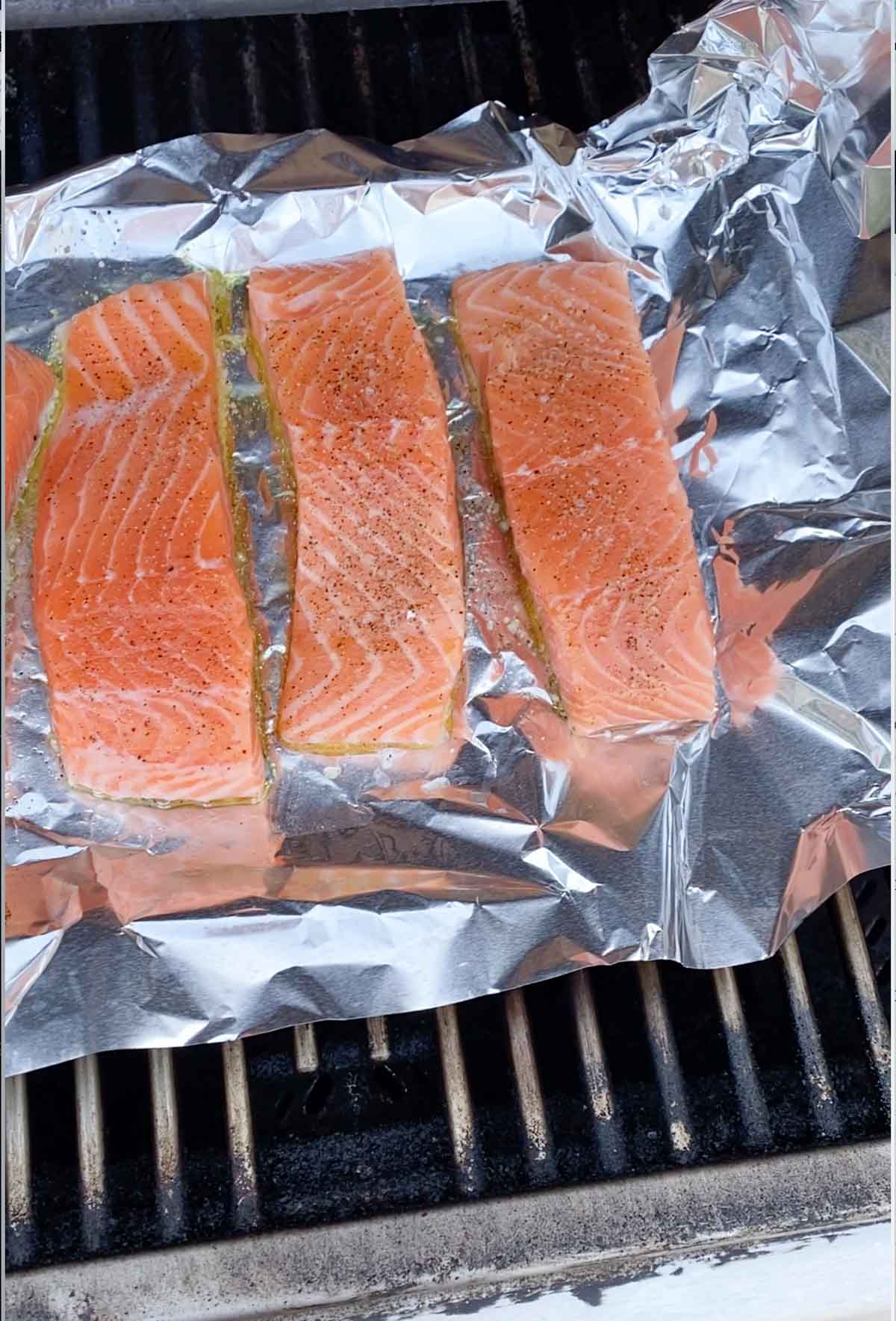 Raw salmon on tin foil on a gas grill.