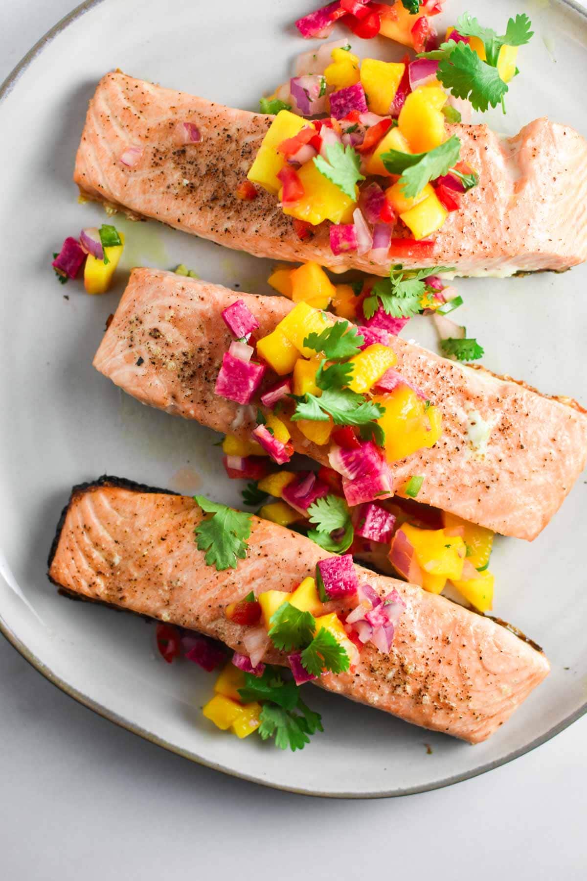 Three filets of grilled salmon topped with a mango salsa on a grey plate.