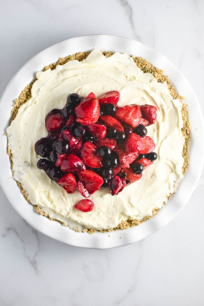 An ice cream pie with berries on top in a white container