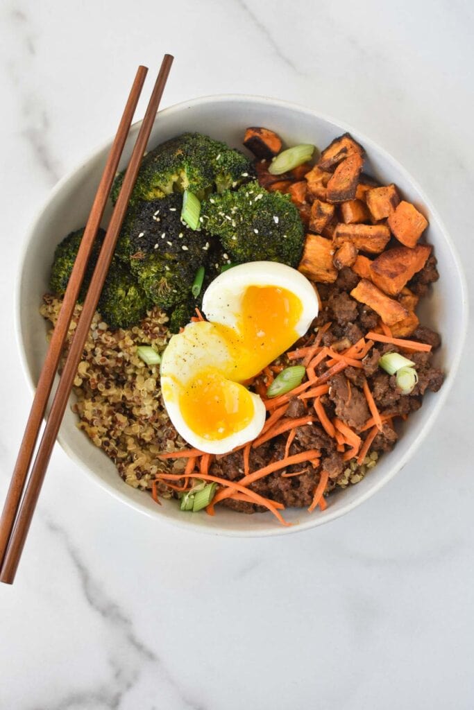 A beef stir fry bowl with a jammy egg on top on a white marble table