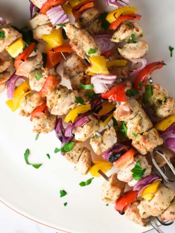 Baked chicken kabobs laid out diagonally on a plate and topped with parsley