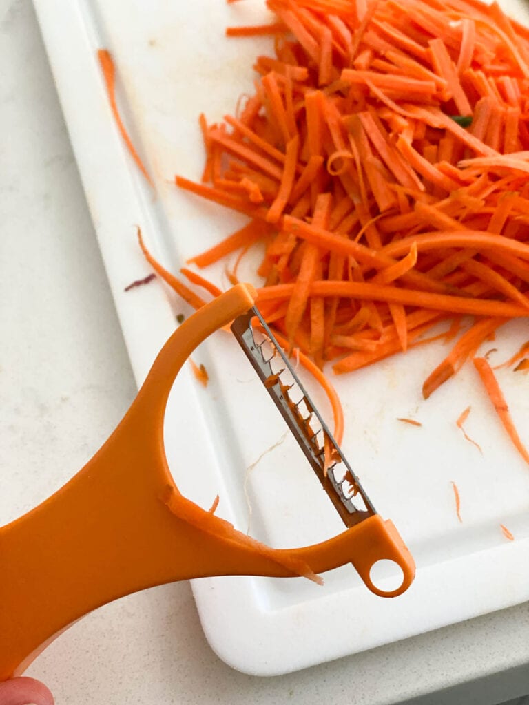 A matchstick peeler with peeled carrots in the background