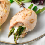Boursin and asparagus stuffed chicken rolled up on a grey plate with a side salad