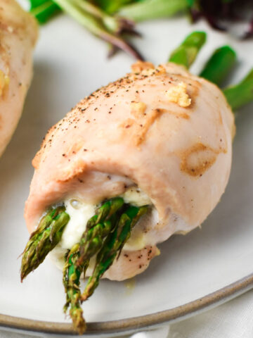 Boursin and asparagus stuffed chicken rolled up on a grey plate with a side salad