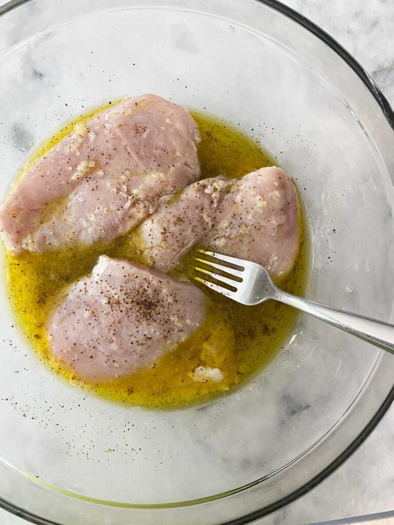3 chicken breasts being marinated in a glass bowl