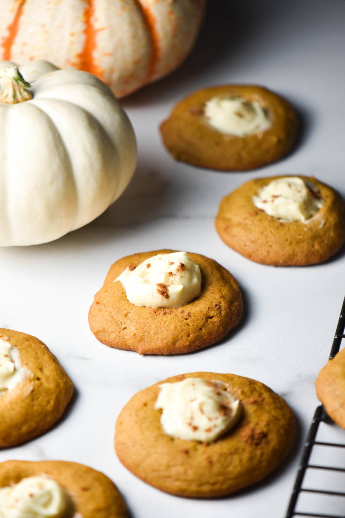 Several cookies topped with cheesecake filling next to a white pumpkin