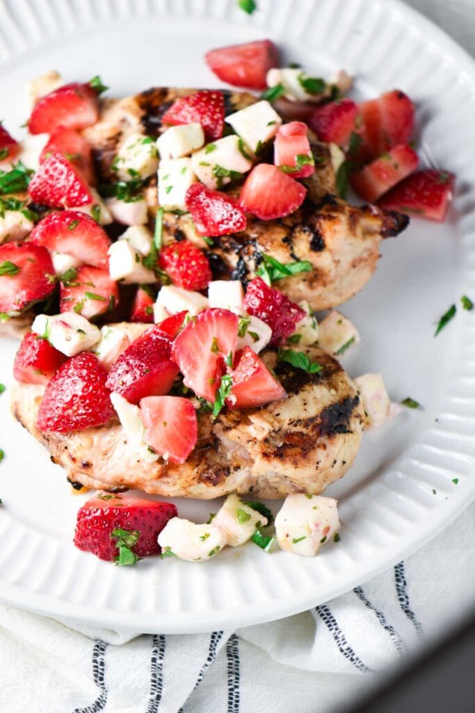 Grilled chicken topped with strawberries, basil, and mozzarella on a white plate