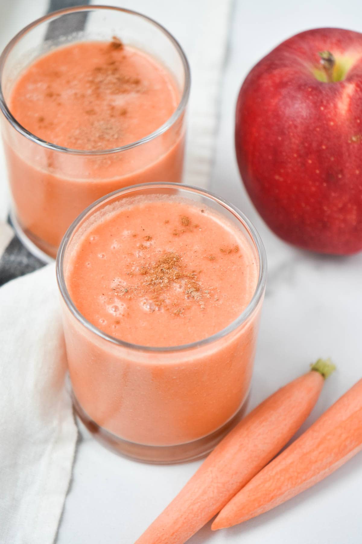 Two carrot apple smoothies with cinnamon on top in glass containers