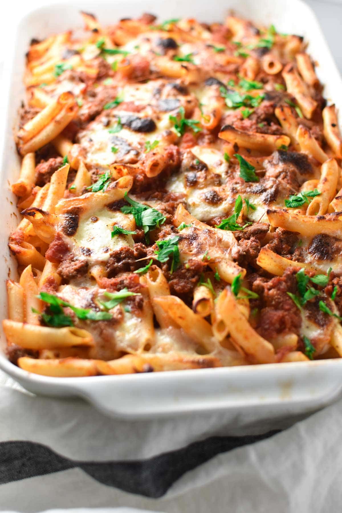 An up close shot of pasta noodles topped with marinara sauce, meat, and cheese in a white baking dish. 