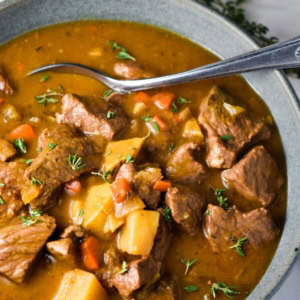 Beef stew without wine in a gray bowl with a spoon and topped with thyme leaves