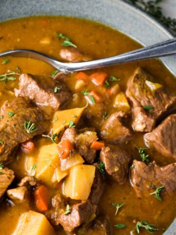 Beef stew without wine in a gray bowl with a spoon and topped with thyme leaves