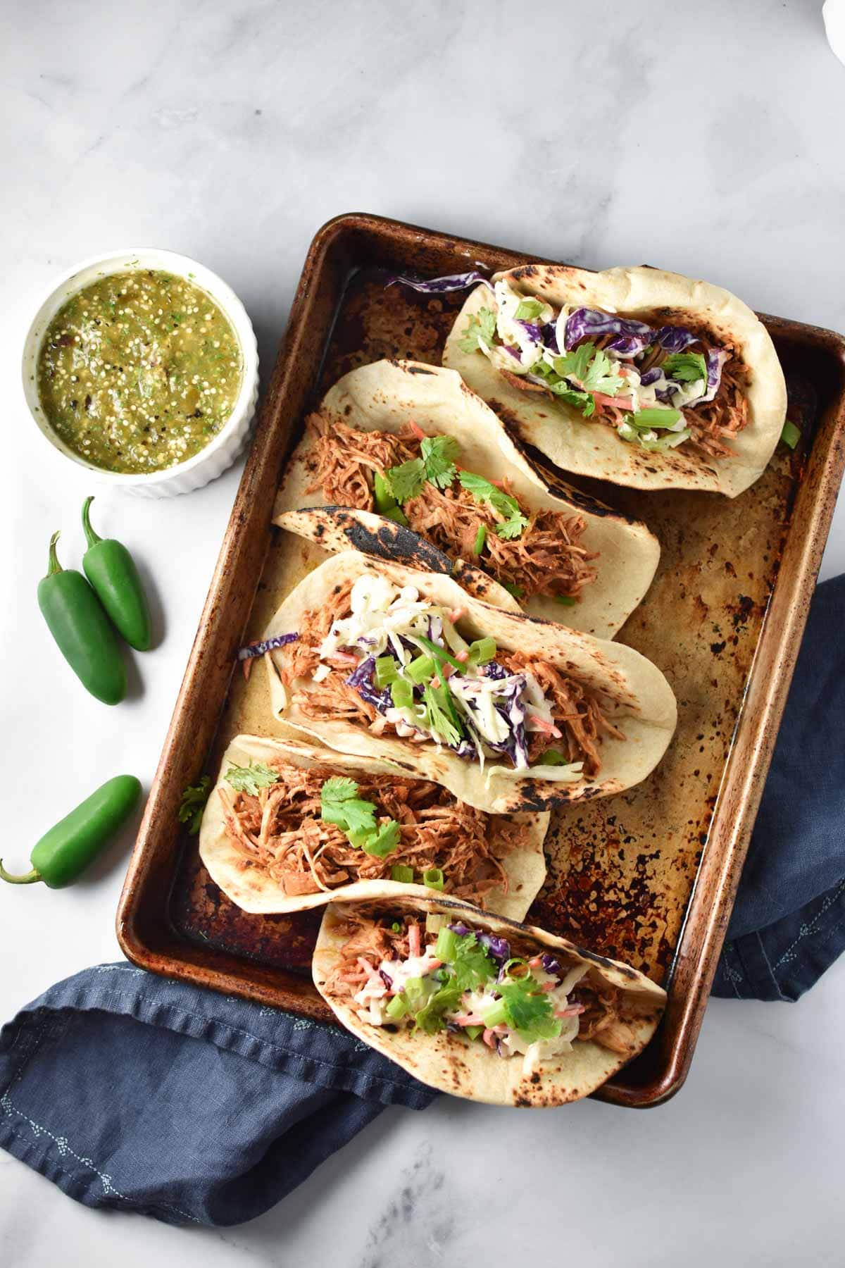 Shredded chicken tinga tacos next to jalapeno peppers