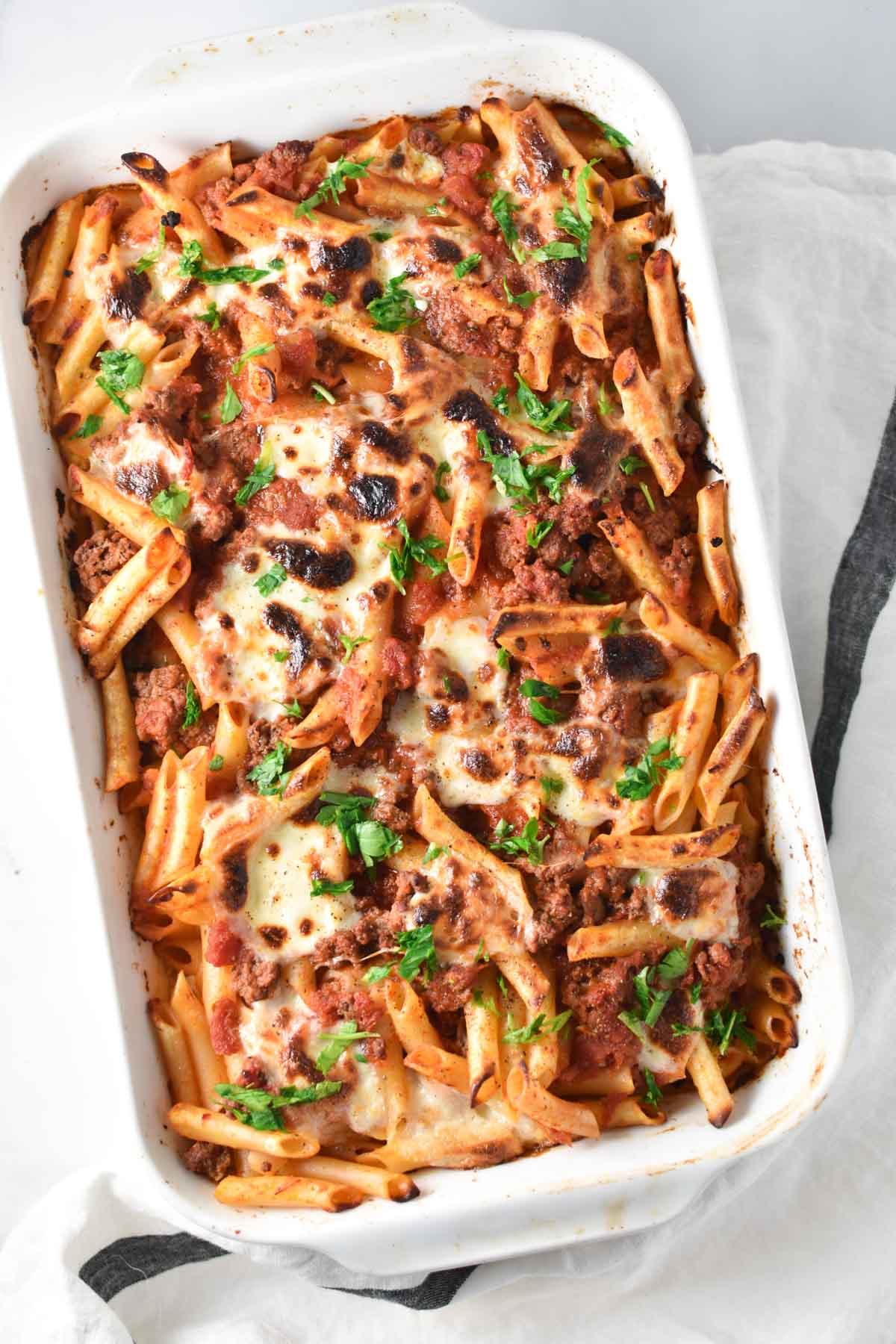 A baking dish filled with lasagna and topped with chopped parsley.