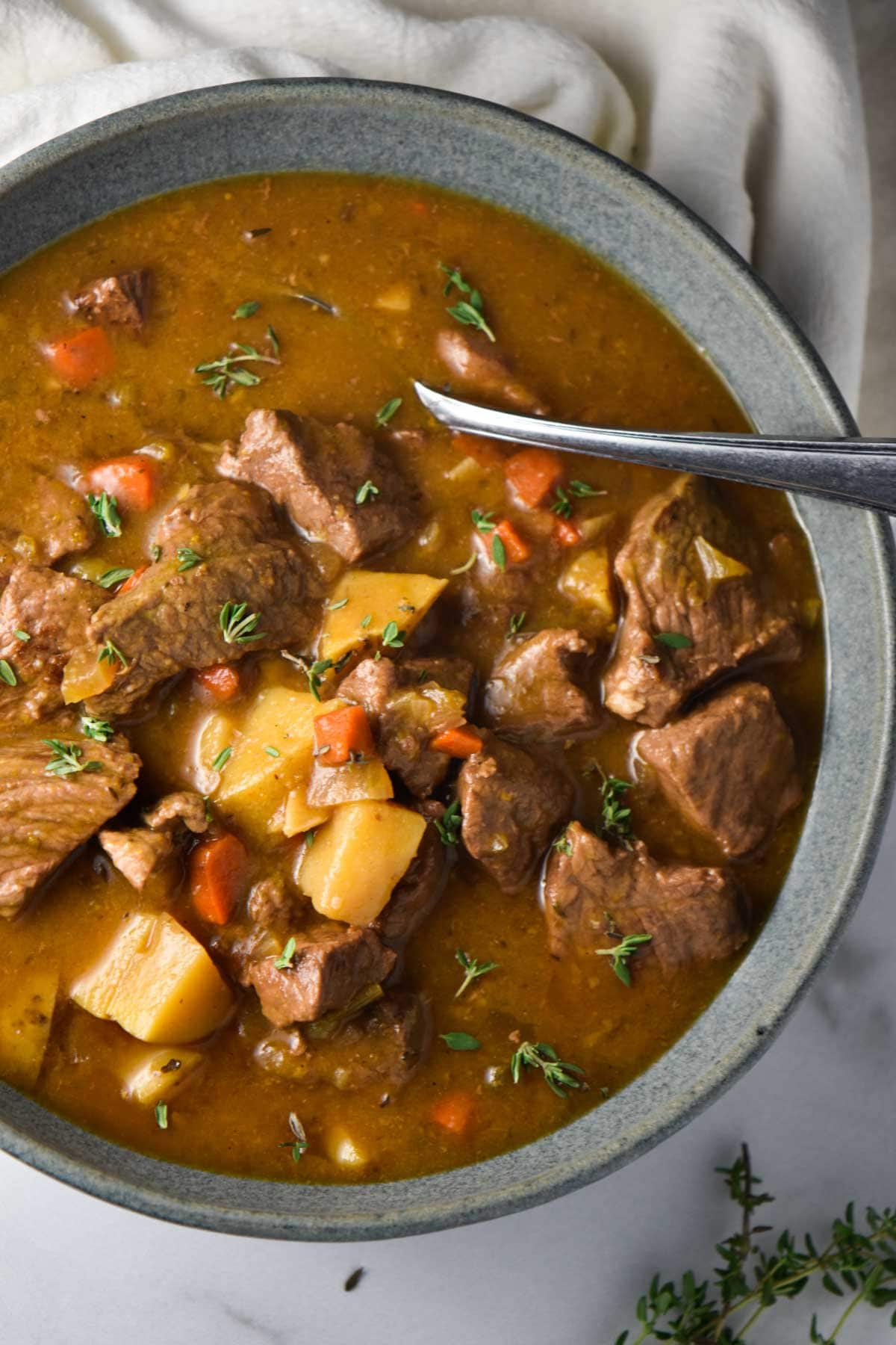 A bowl of beef stew with carrots and potatoes on a kitchen towel