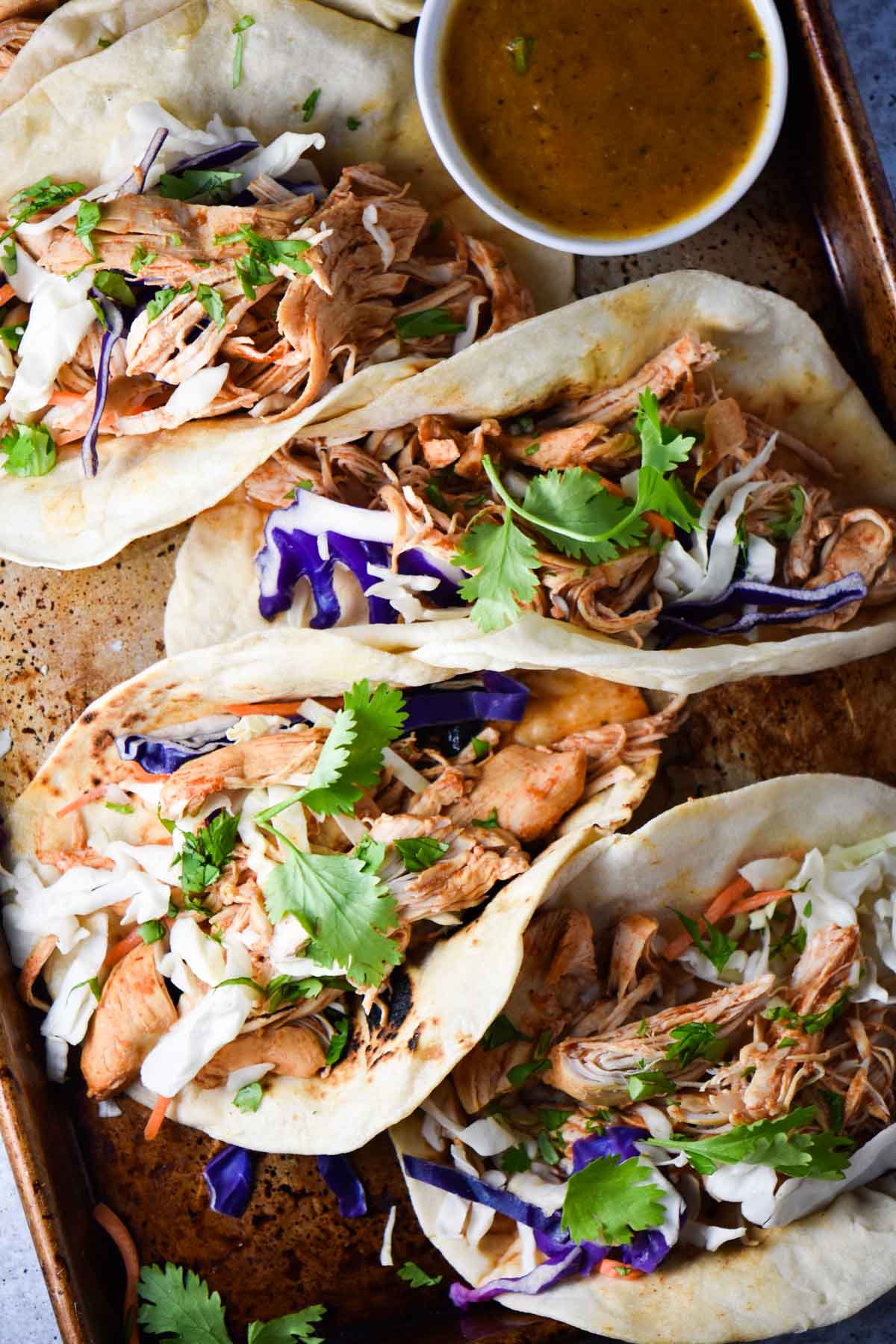 Shredded chicken tacos on a sheet pan with red salsa