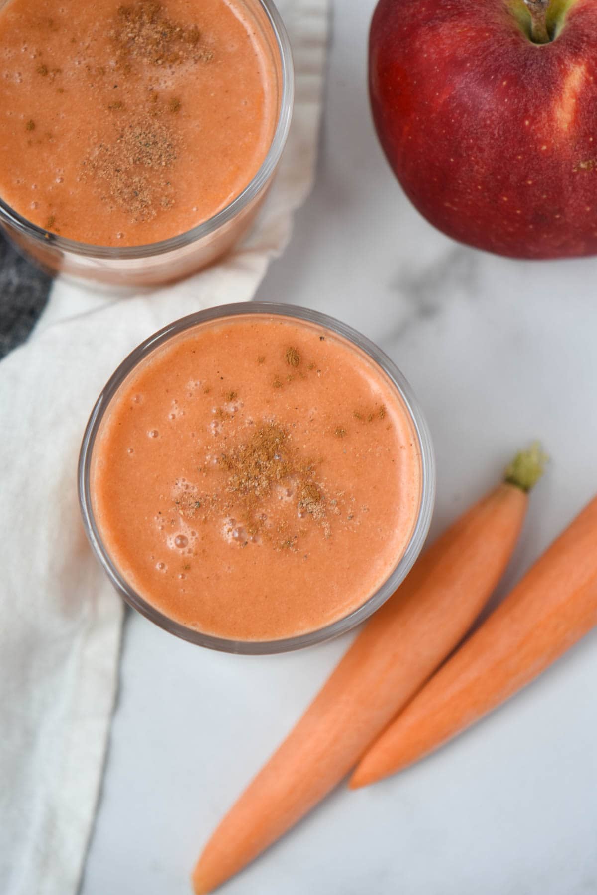 An orange colored smoothie on a table next to carrots