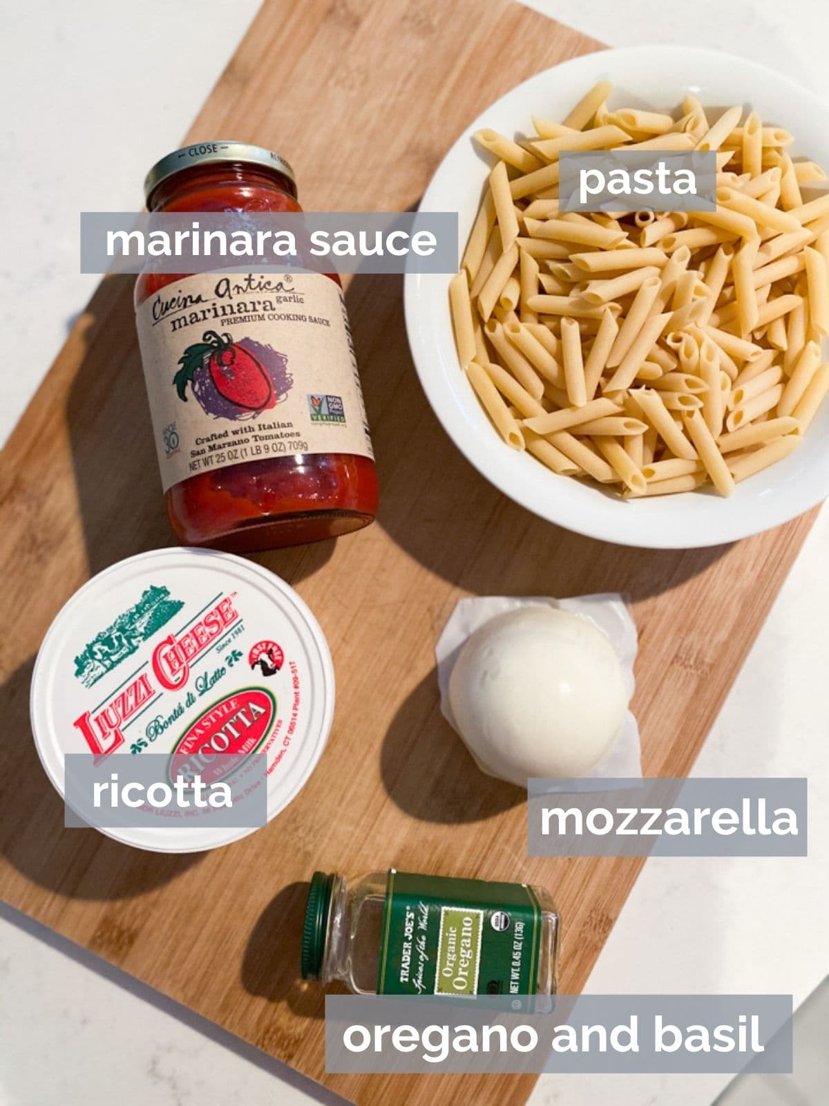 Ricotta, mozzarella, pasta, and marinara sauce on a wood cutting board.