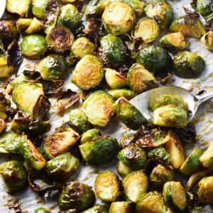 Roasted bang bang brussels sprouts on a baking sheet with a spoon flipping one