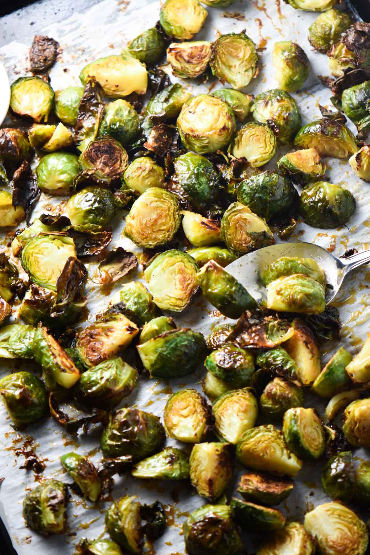 Roasted bang bang brussels sprouts on a baking sheet with a spoon flipping one.