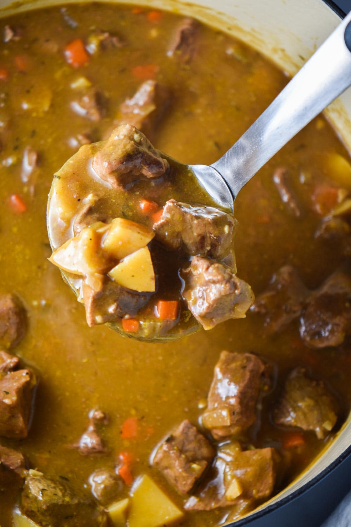 A ladle spooning out stew from dutch oven