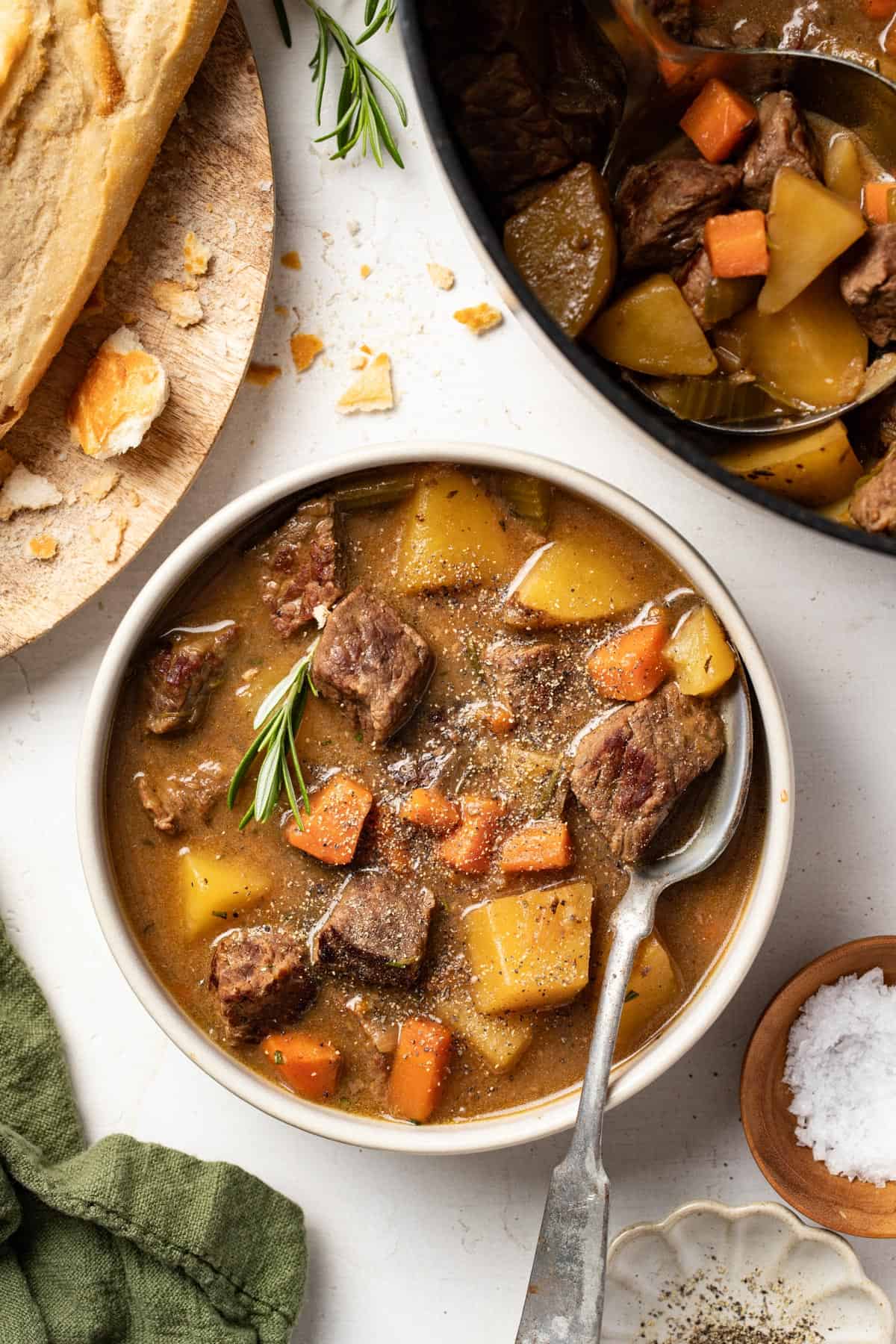 Beef stew in a bowl next to a baguette.