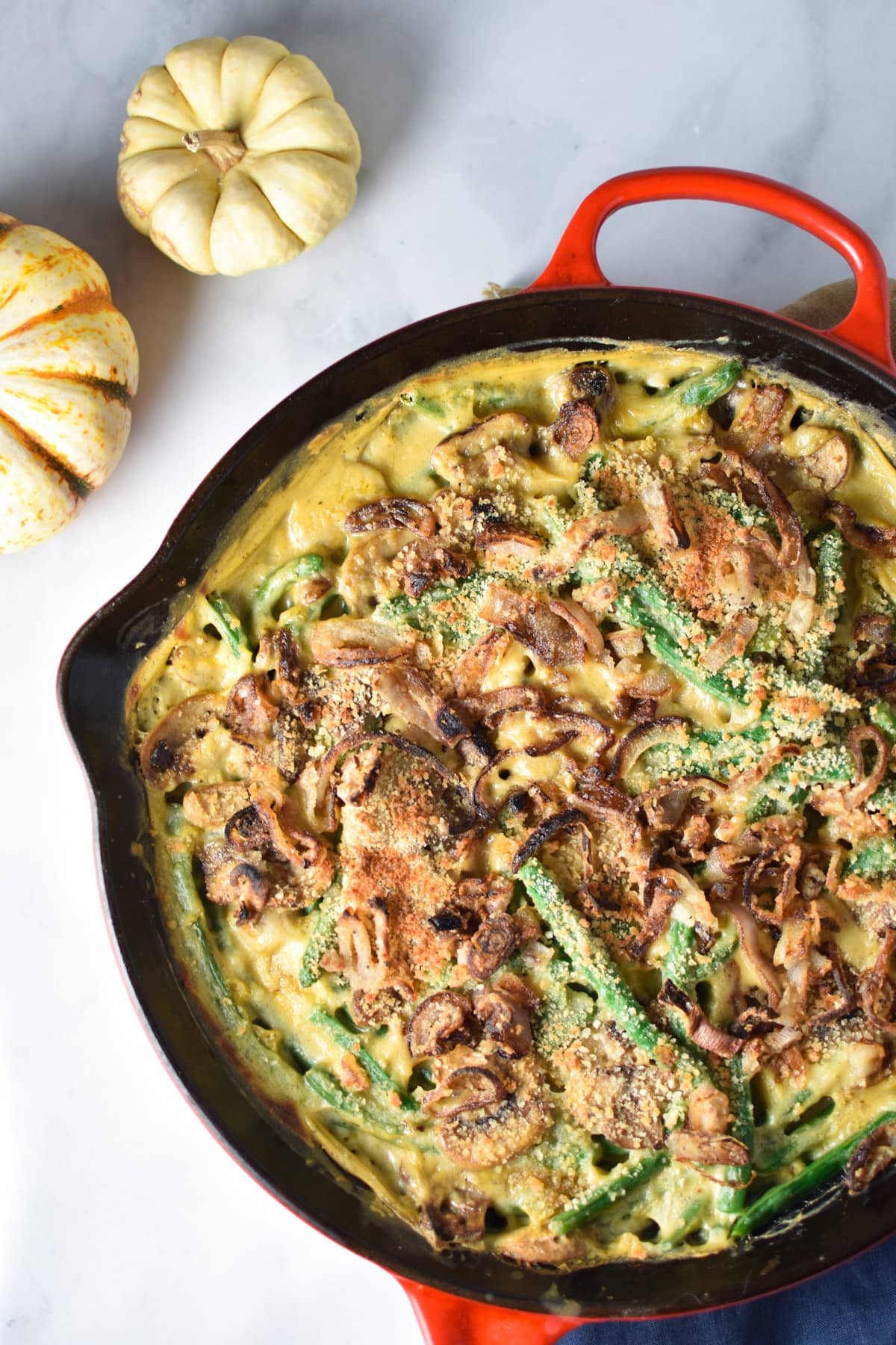 A pan with green bean casserole next to two pumpkins.