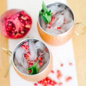 Two pomegranate mojito mocktails on a wood table with mint and a fresh pomegranate