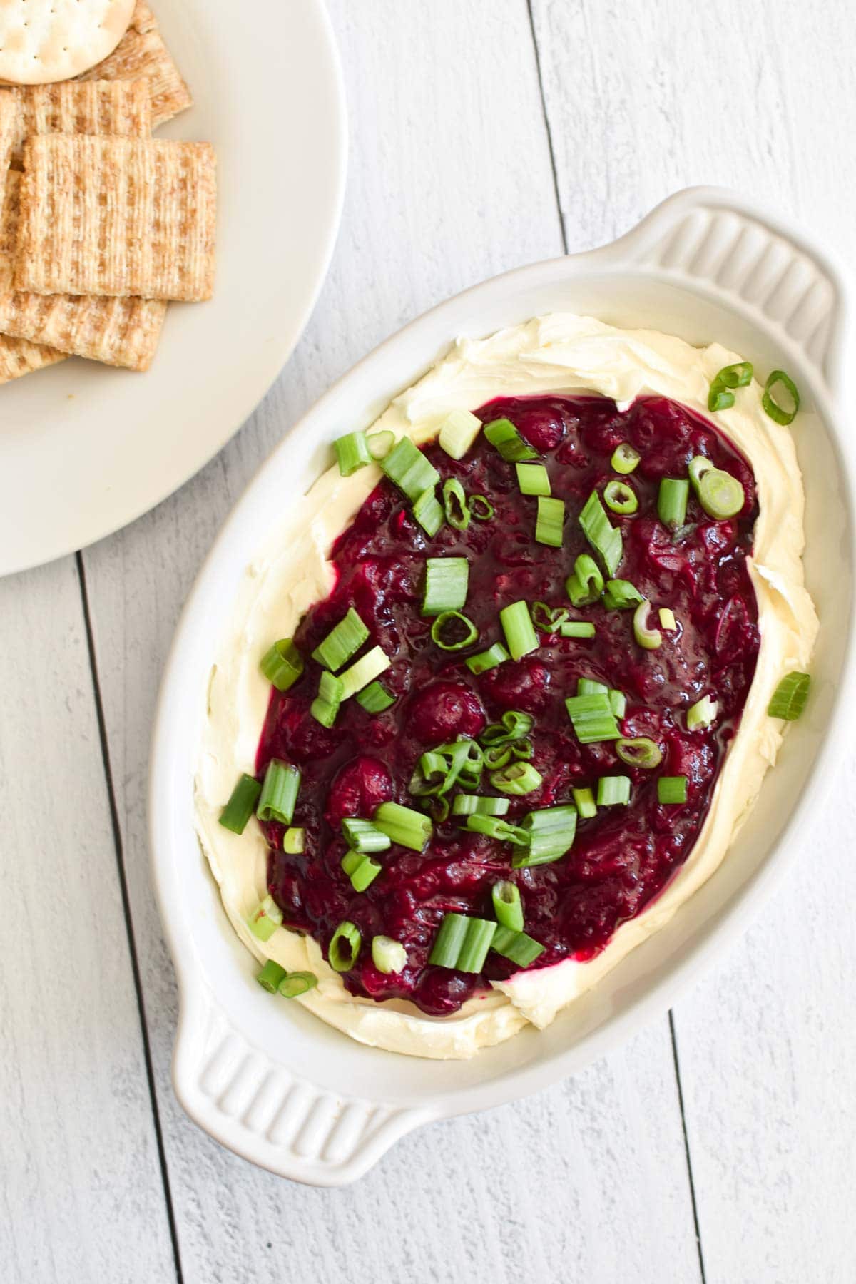 A white bowl filled with cranberry jalapeno dip next to wheat crackers on a plate