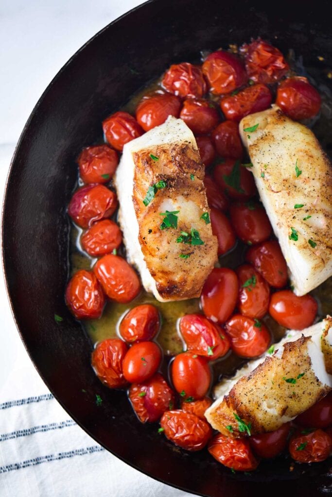 Three pan seared sea bass in a frying pan with cherry tomatoes and a white wine sauce