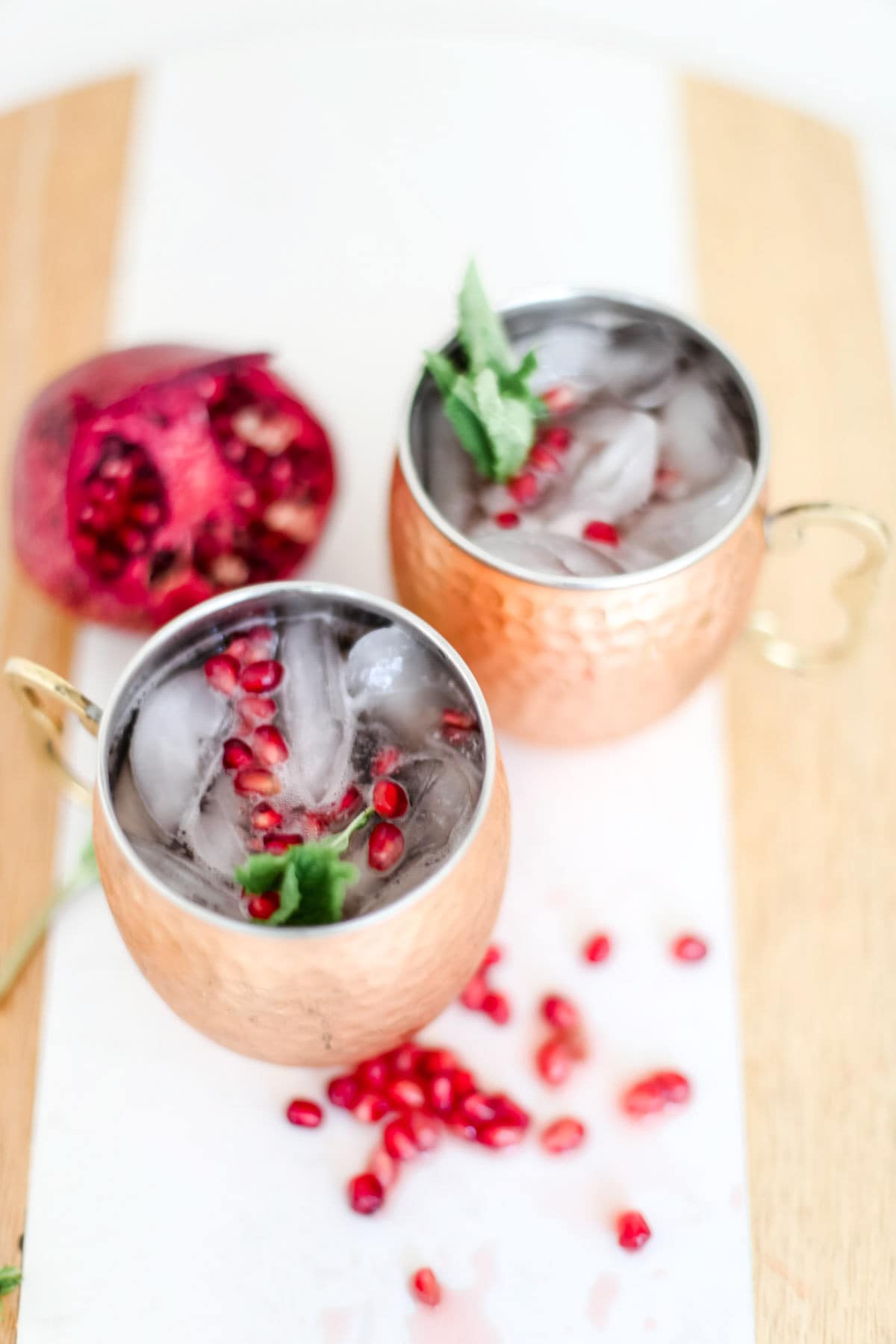 Two glasses of pomegranate mocktails next to a whole pomegranate and seeds.