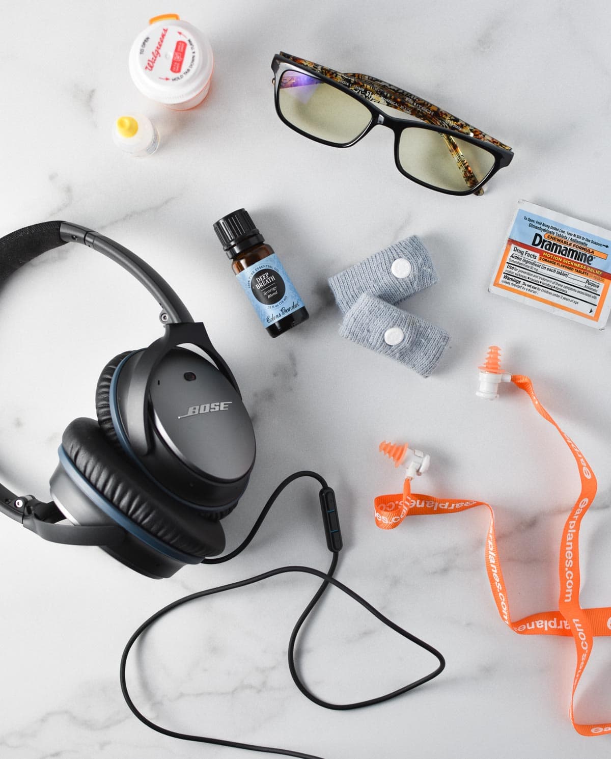 Headphones, sea bands, migraine glasses, earplanes, and timolol eye drops on a white table