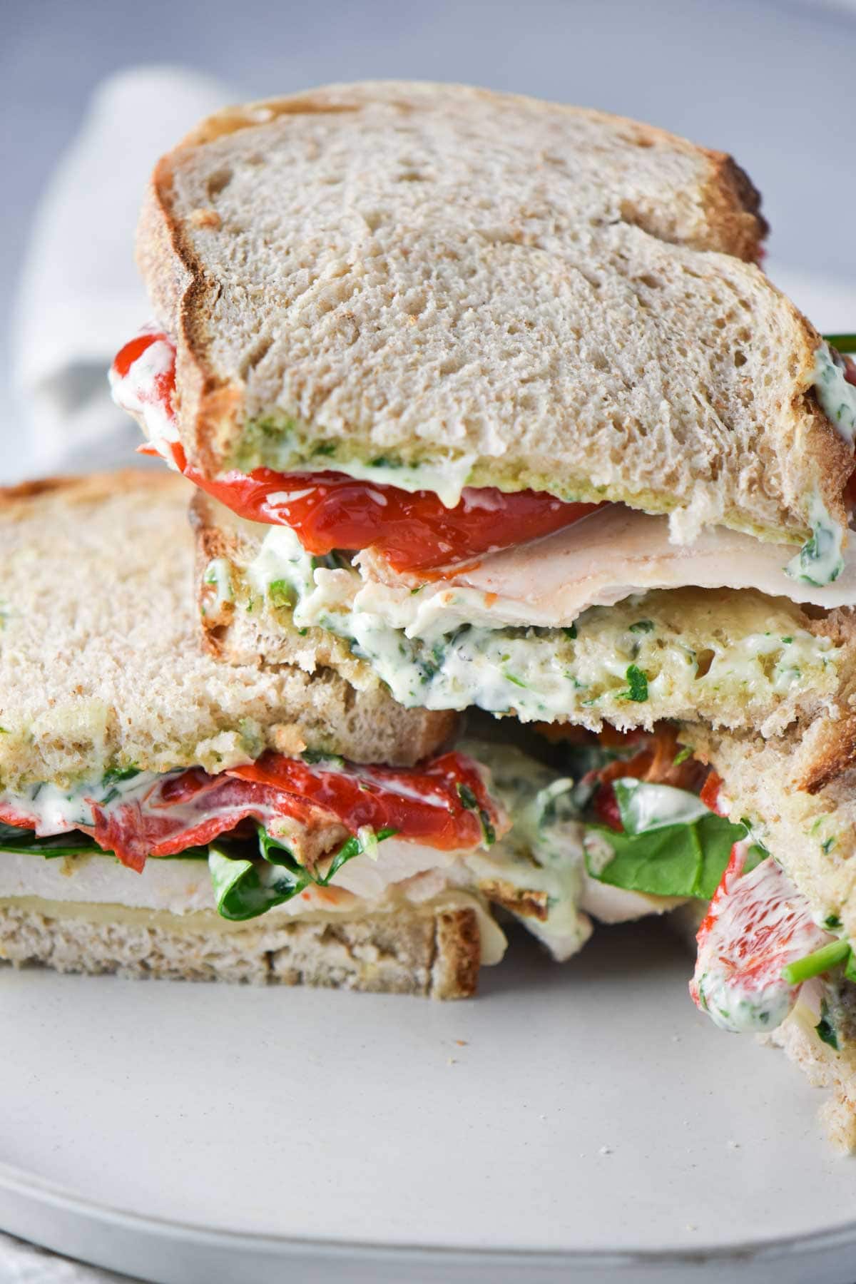 Three halves of a turkey sandwich with pesto mayo and red pepper on top of each other.
