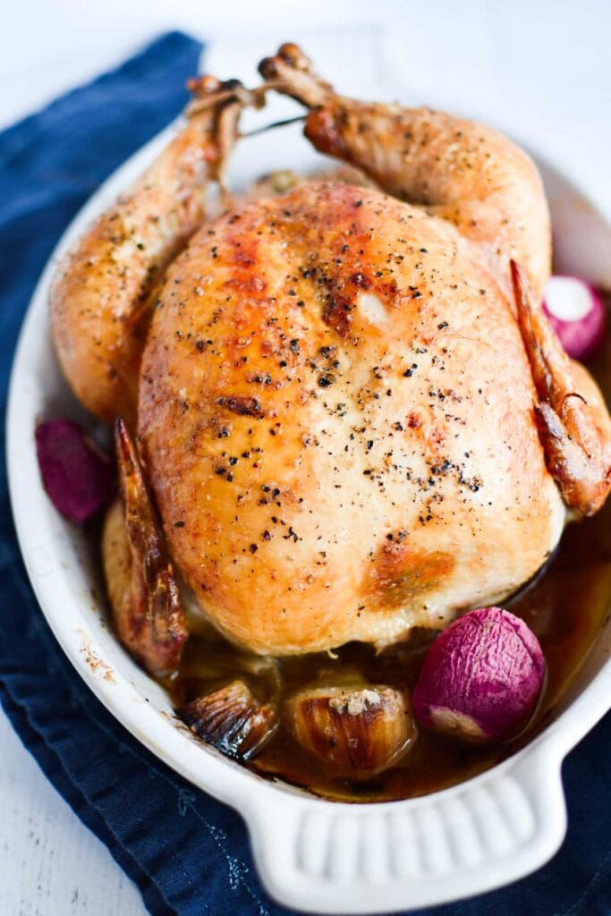 A whole roasted chicken in a baking dish with radishes.