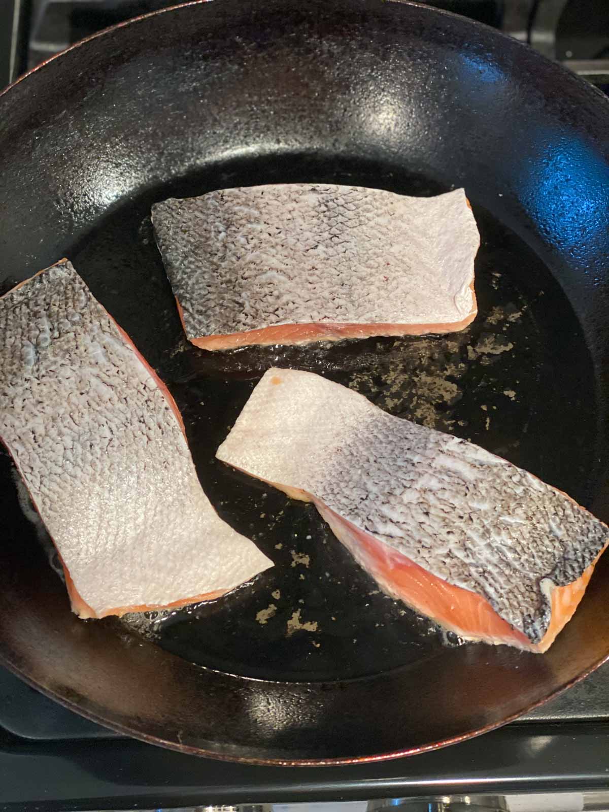 Salmon fillets being seared skin side up in a cast iron pan.