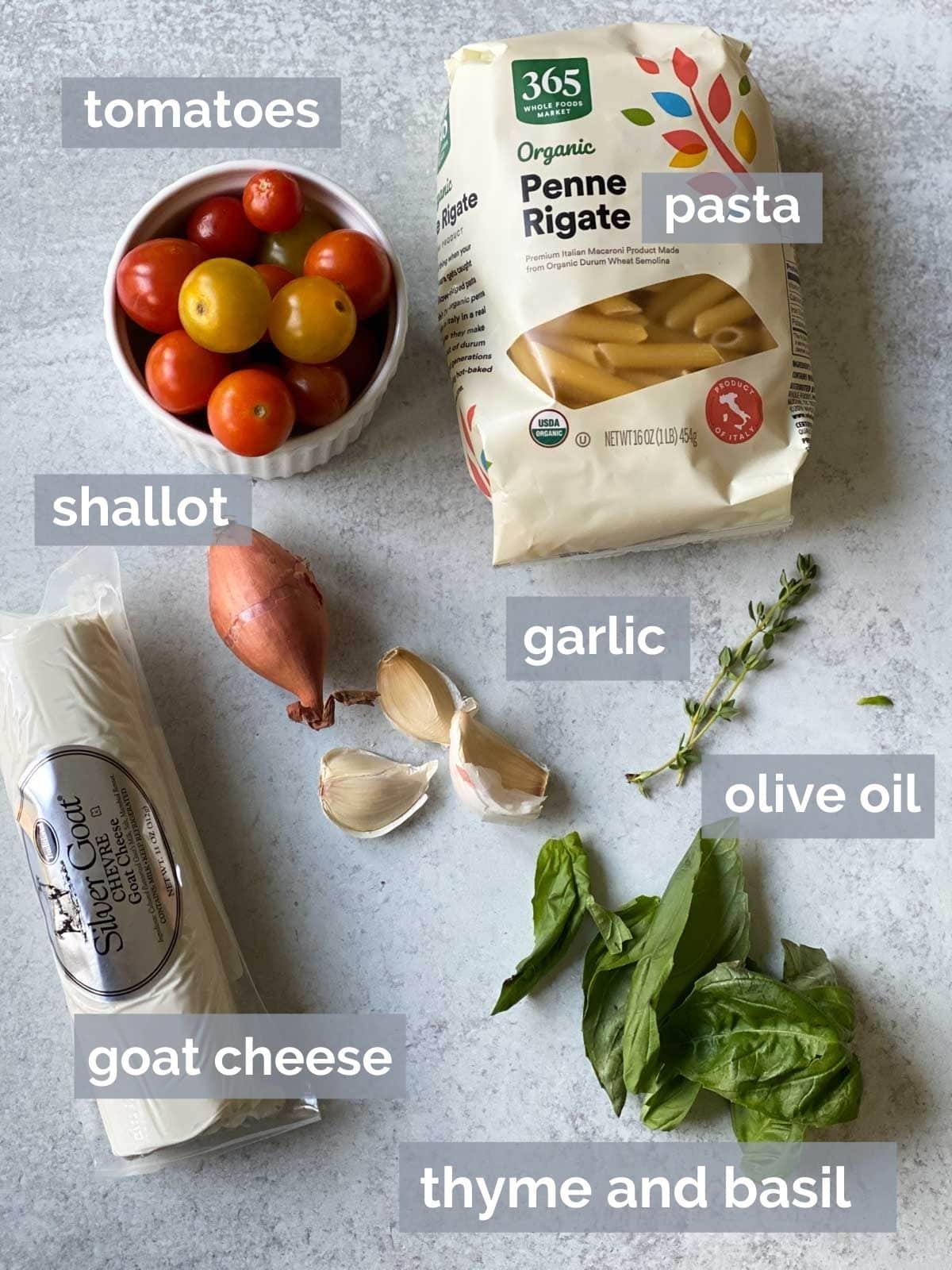 Tomatoes, pasta, goat cheese, basil, and garlic on a table.