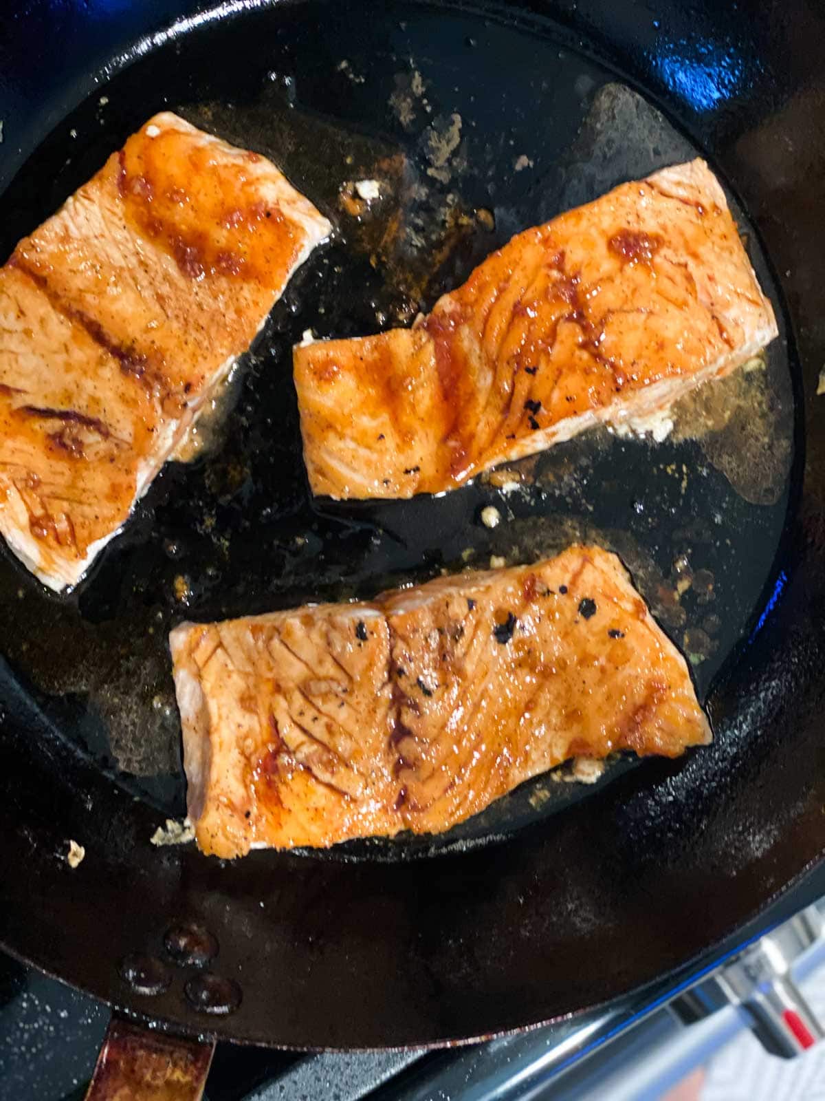 Three salmon filets being pan-fried and brushed with teriyaki sauce