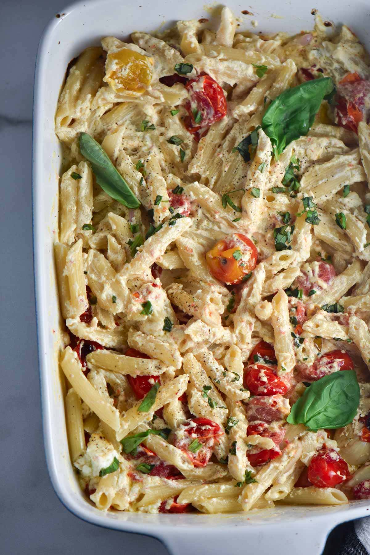 A baking dish filled with creamy tik tok pasta with goat cheese topped with basil