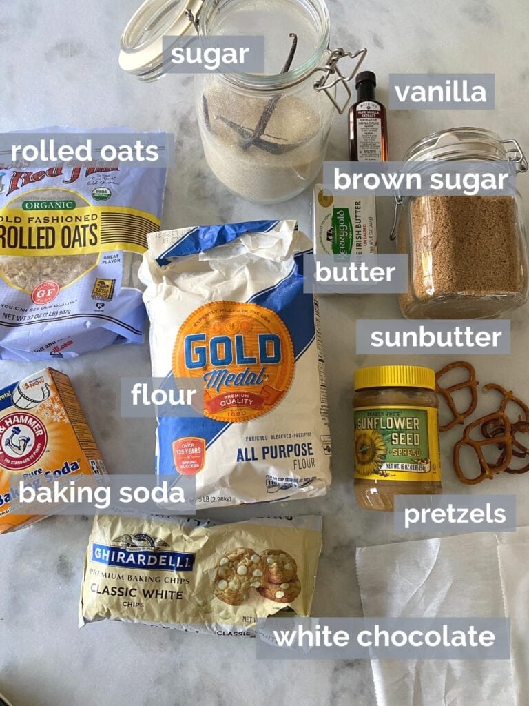 Flour, oats, sugar, white chocolate, pretzels, sunbutter and baking soda on a white table
