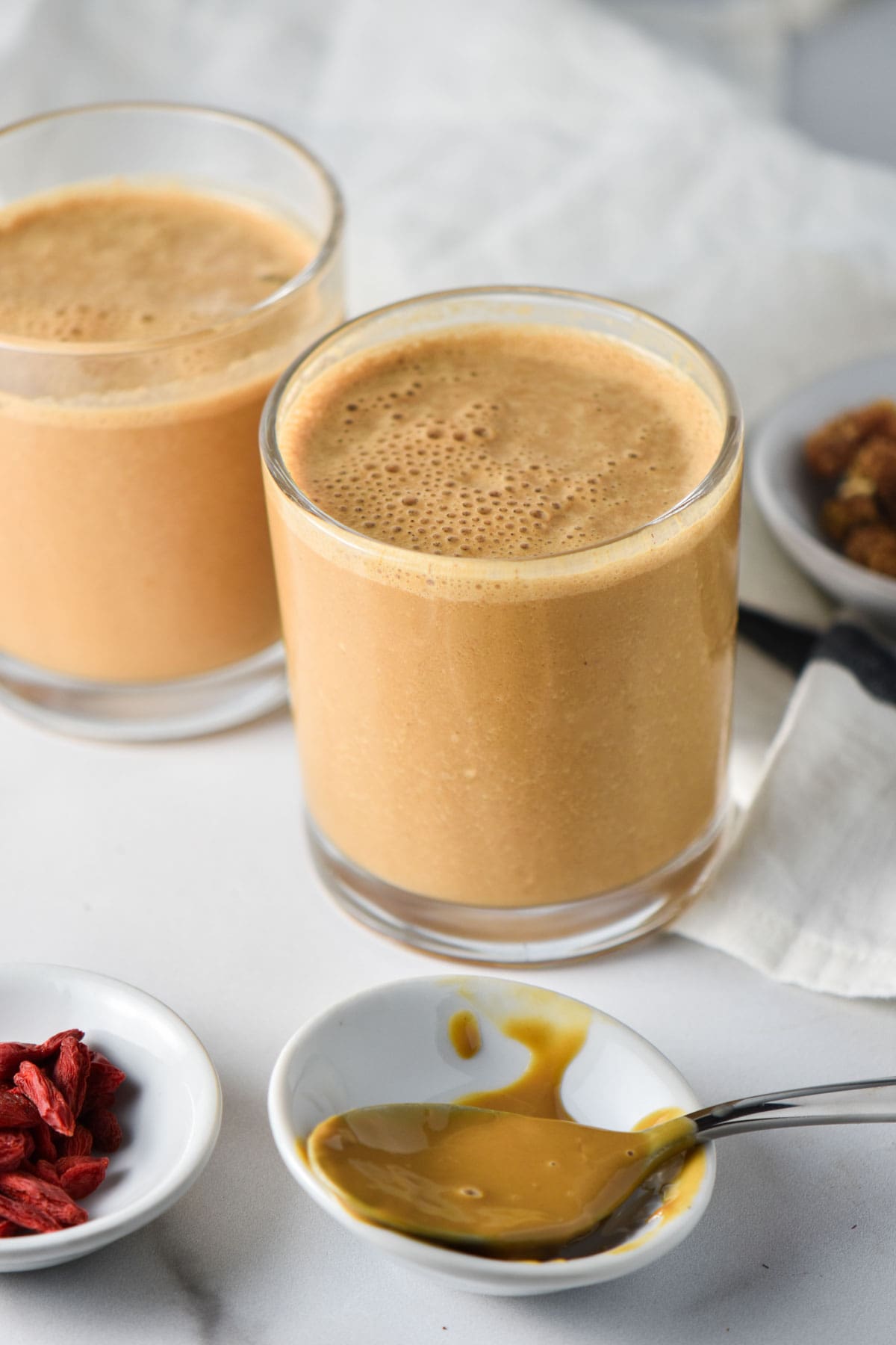 Two maca smoothies next to a spoon with sunbutter and a white cloth