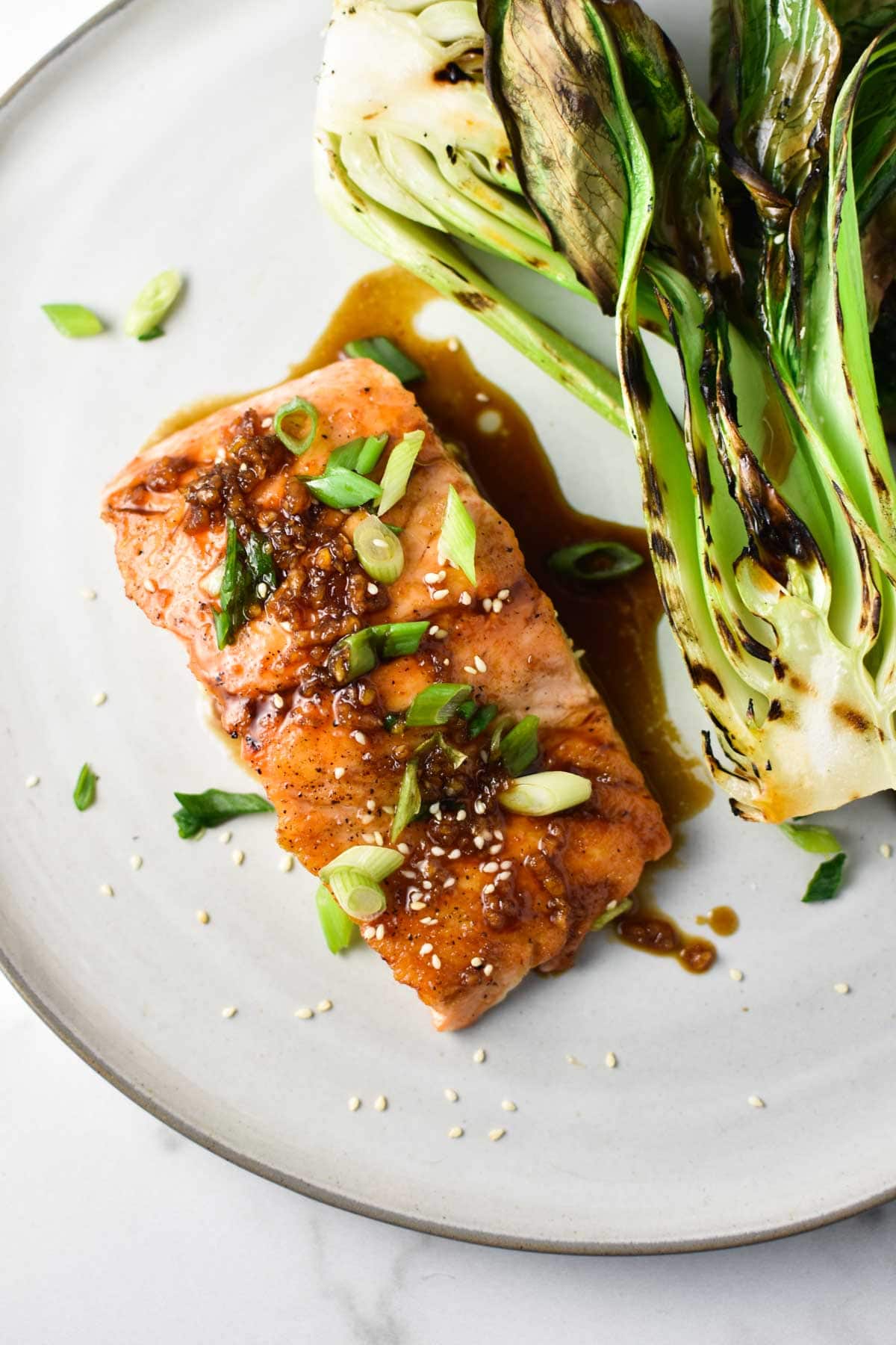 A fillet of salmon brushed with a teriyaki glaze next to a grilled bok choy.