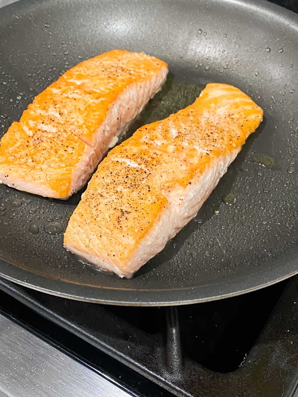 Two filets of salmon being pan seared in a nonstick pan