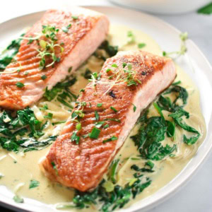 Two salmon with spinach cream sauce on a white plate