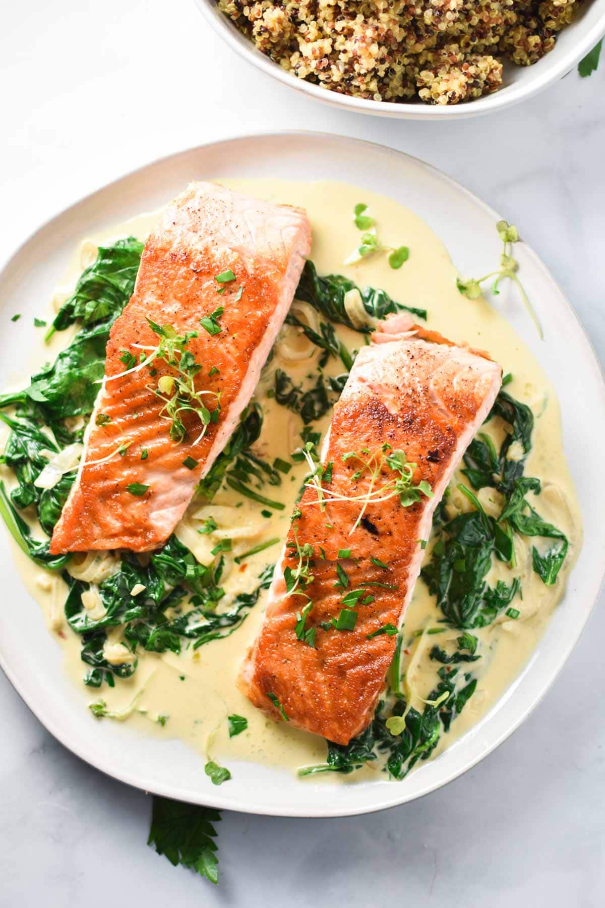Pan seared salmon on a white plate with creamy spinach and quinoa.