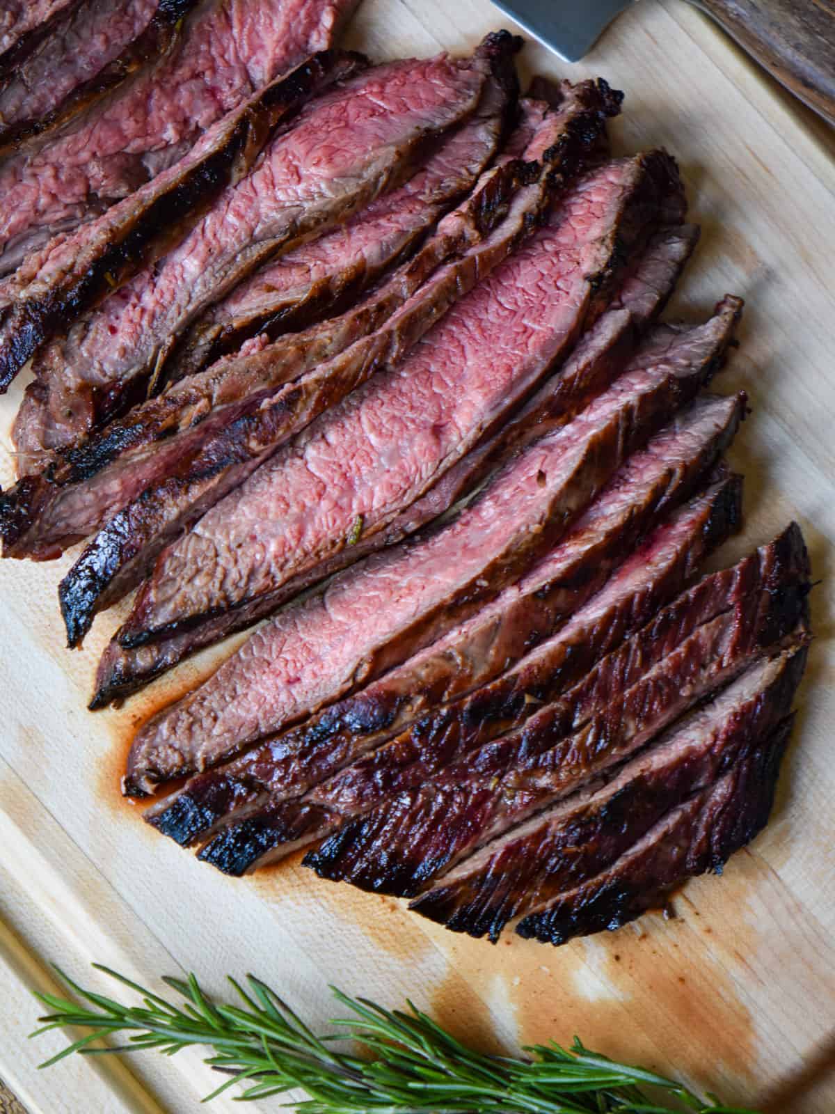 Sliced flank steak on a cutting board showing a medium pink inside.