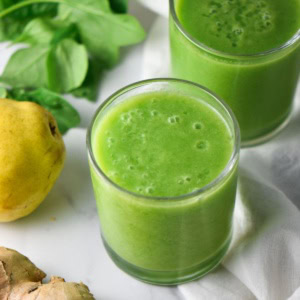 A cup with an anti inflammatory green smoothie next to a pear.