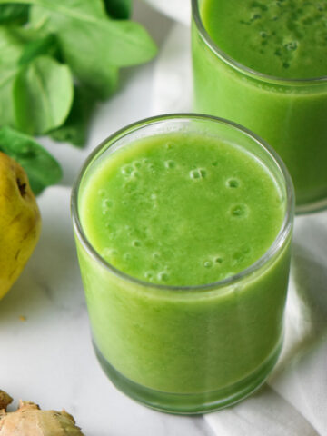 A cup with an anti inflammatory green smoothie next to a pear.